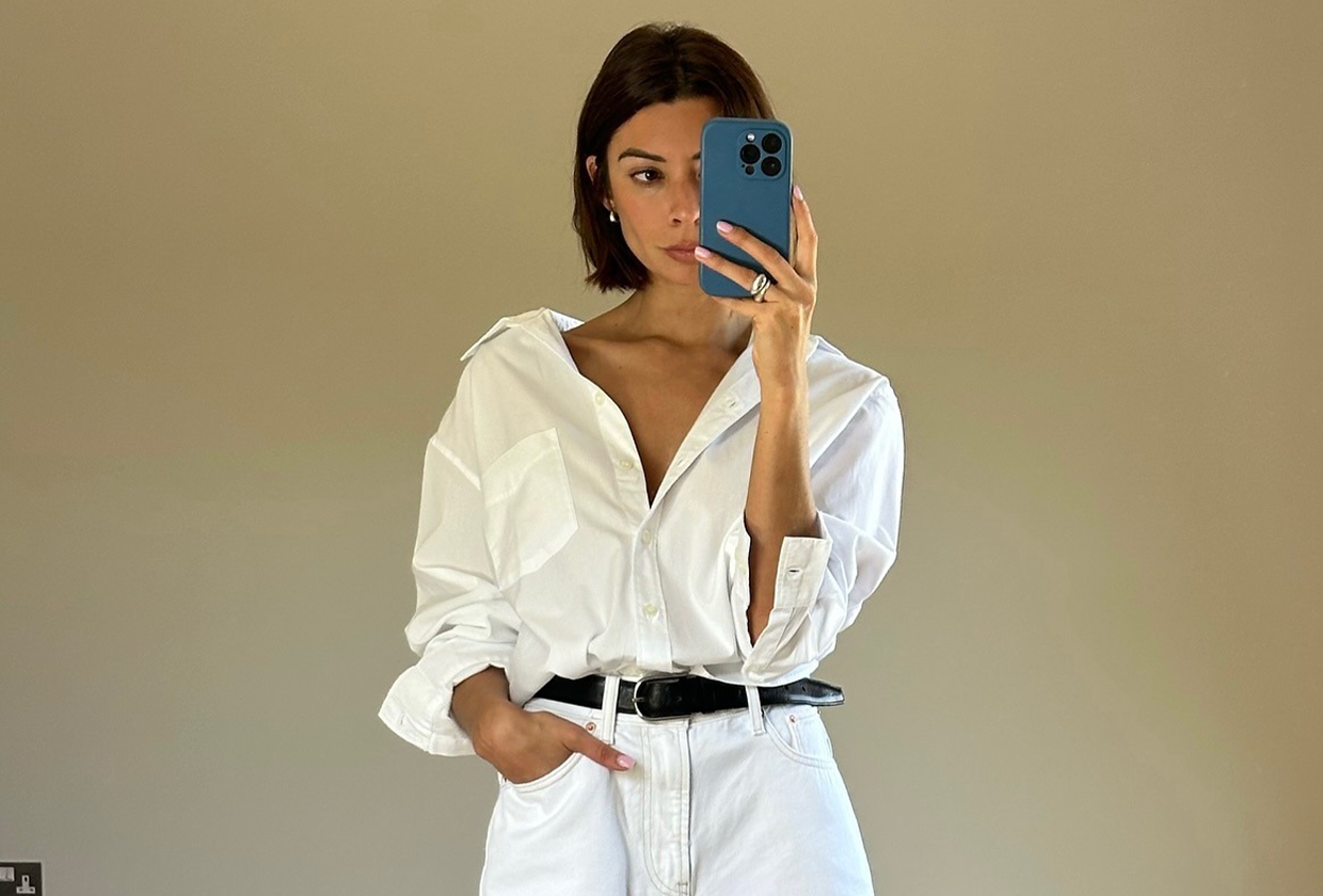 Woman wearing white button down, black belt, and white bermuda denim shorts.
