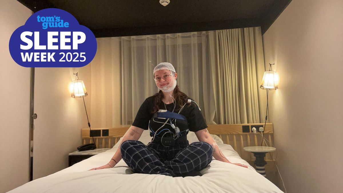 The Tom&#039;s Guide Sleep Features Editor sitting cross legged on a hotel bed with wires strapped to her body and head to monitor her sleep