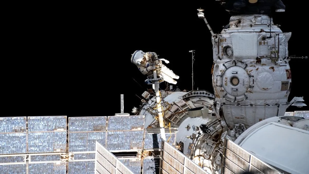 an astronaut in a white spacesuit takes a spacewalk outside a space station