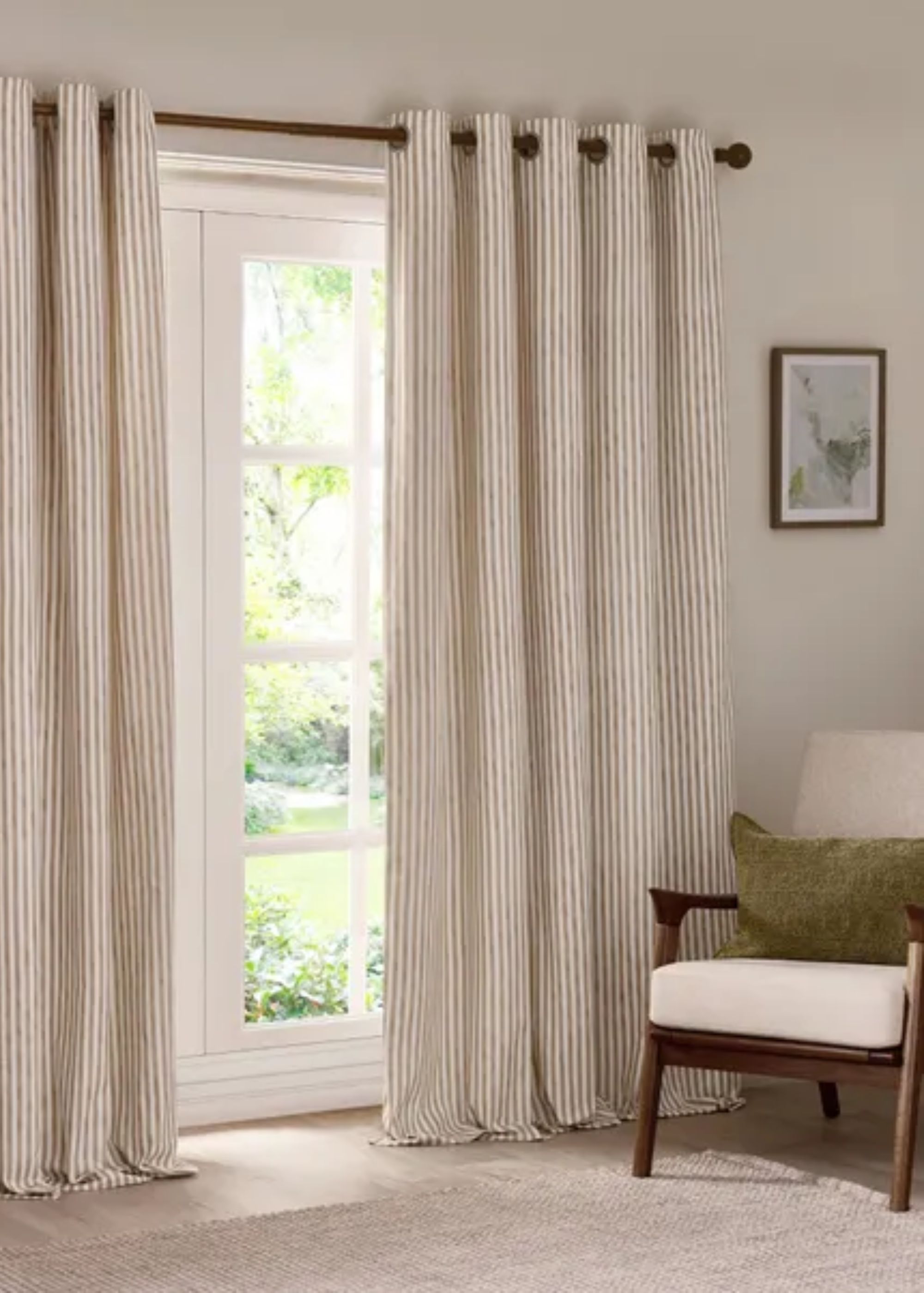 Striped curtains in a living room with a chair in the corner of the room with a deep green cushion. Above the chair is artwork hanging on the wall