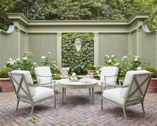 A garden with outdoor seating area, green and white furniture, and sage green trellis