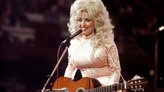 American singer, songwriter and actress Dolly Parton, performs with a guitar, 1976. 