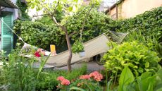 A woman lies in a hammock in her garden, reading a book. She looks relaxed.