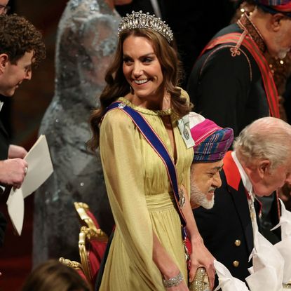 Princess Kate wearing a yellow gown and tiara standing at a table