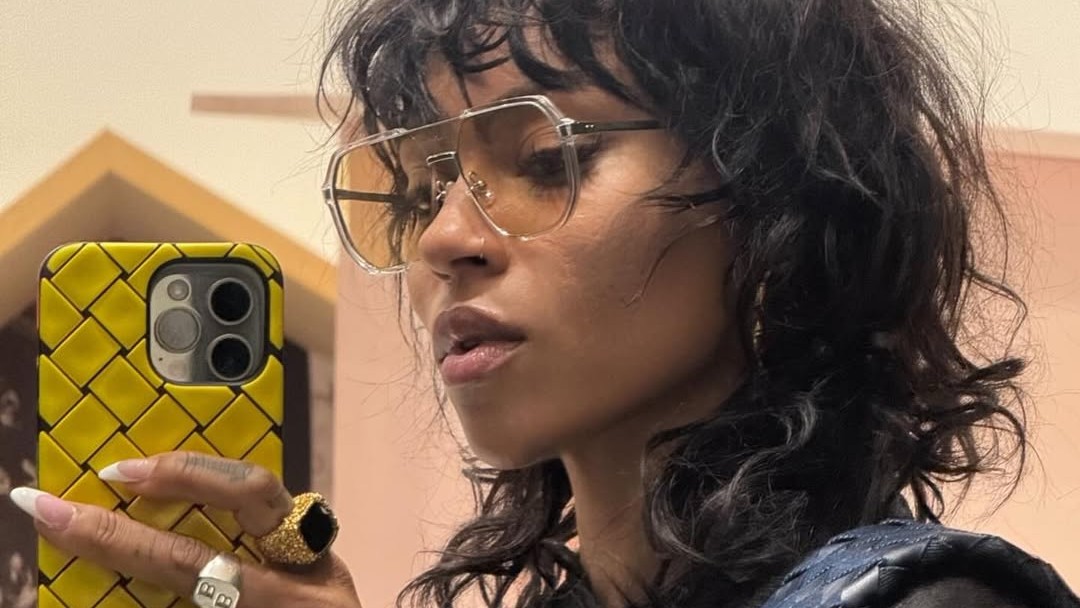 A shaggy bob haircut by Karen Miller on a woman holding up a yellow phone with gold rings