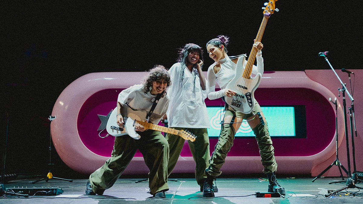 Darumas playing guitar and bass on stage, against a retro-futuristic pink background