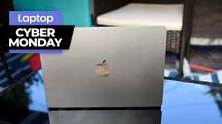 MacBook Air M2 sitting on a glass coffee table with the lid facing the camera and a Cyber Monday banner in the upper-left corner