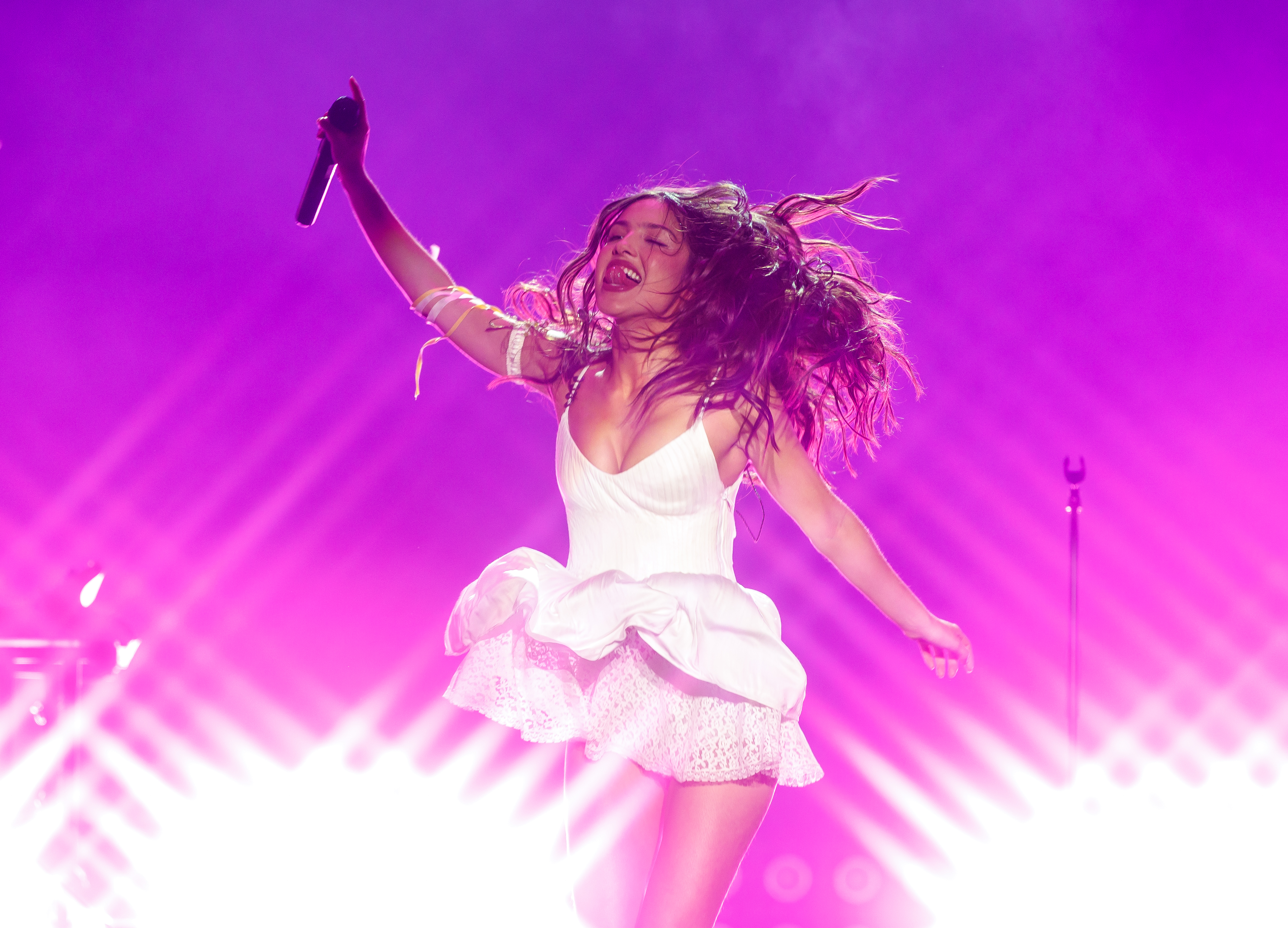 Olivia Rodrigo wears a white lacy dress with a white daisy in her hair to perform at Daisy Chain Fields