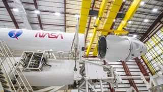 A white SpaceX Endeavour Dragon capsule is mated to its Falcon 9 rocket with NASA logos on white backgrounds.