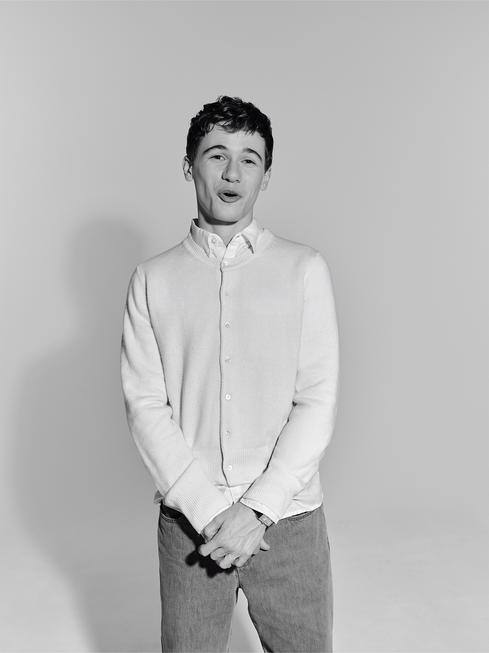 Actor Sam Nivola, photographed by JJ Geiger for Who What Wear. He is wearing a white button-down shirt and khaki trousers with a yellow cardigan.