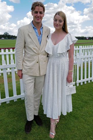 Alexander Ogilvy wearing a tan suit standing with his sister Flora Vesterberg wearing a white dress in front of a white picket fence