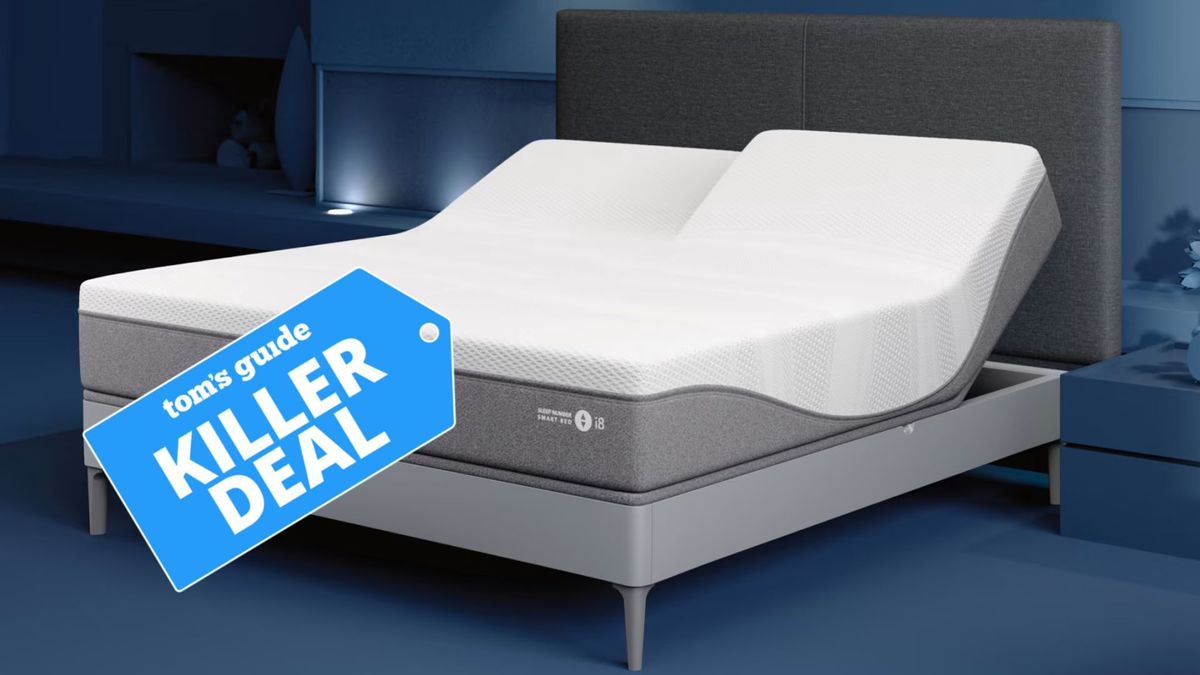 The image shows the SleepNumber i8 smart mattress on a grey bed frame in a blue bedroom