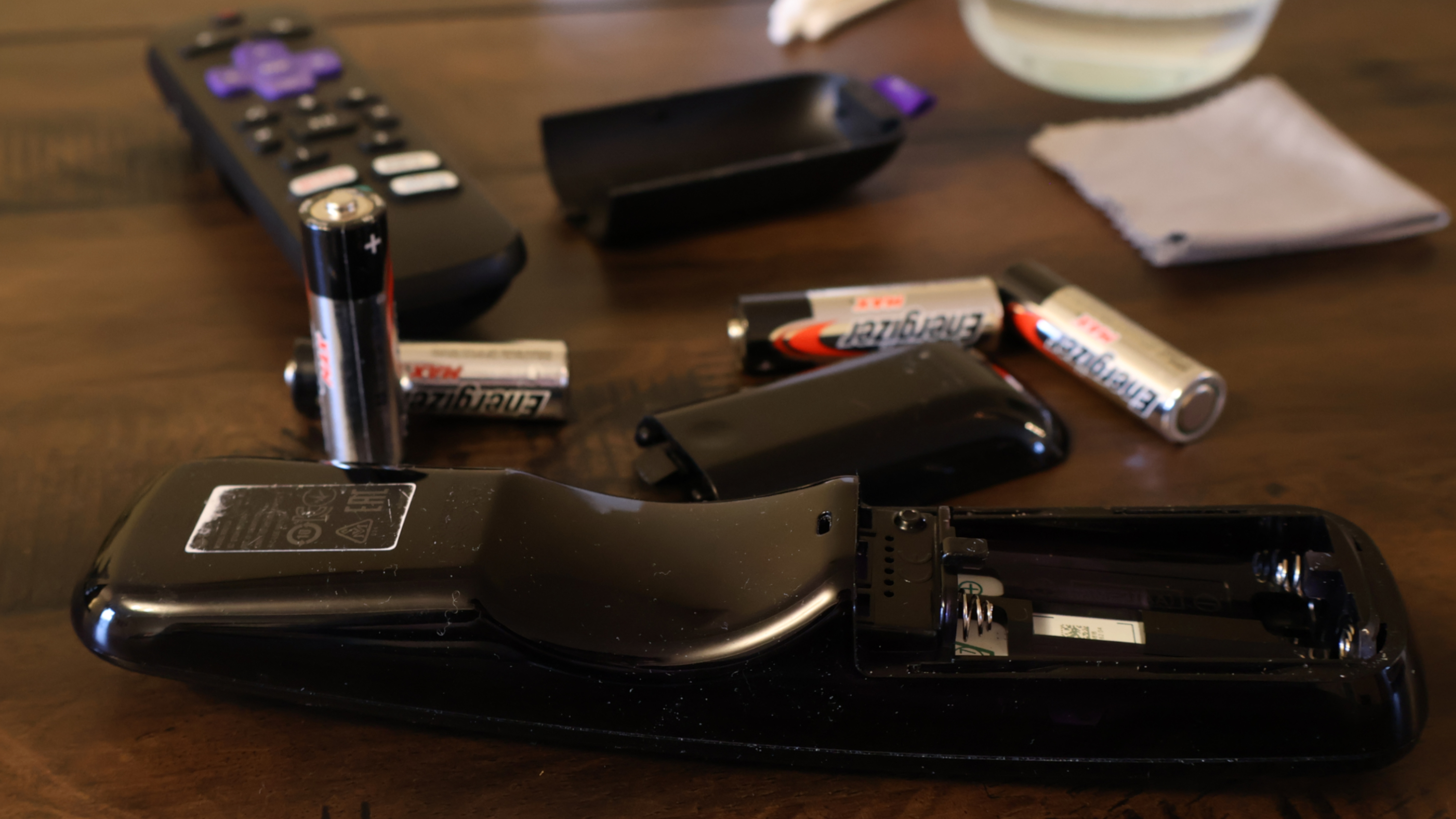 Two remote controls on the surface of a wooden table with their AA-sized batteries removed