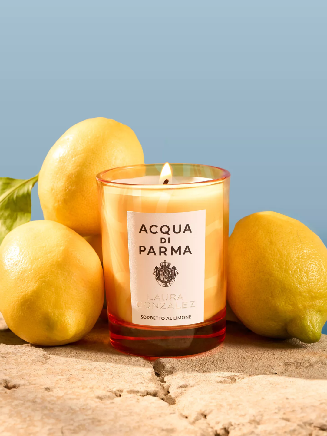 A yellow glass candle surrounded by lemons from Acqua di Parma