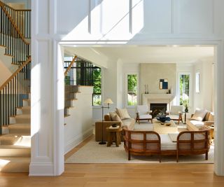 hall and stairs view to living room with taupe sofas white walls, wooden floors and furniture and fireplace