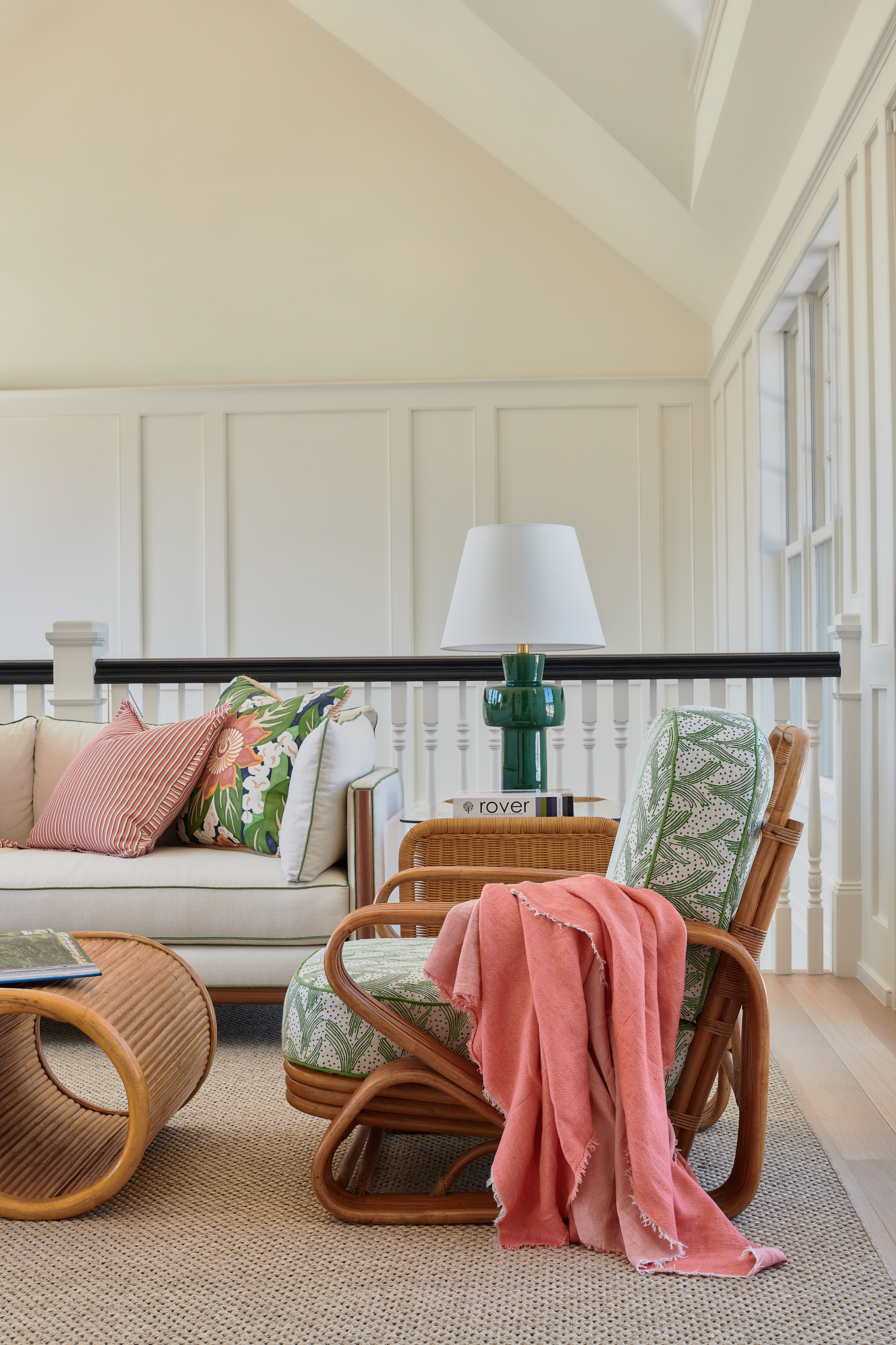 A living room vignette spotlighting a wicker or bamboo chair with a green and white cushion, draped with a pink blanket.