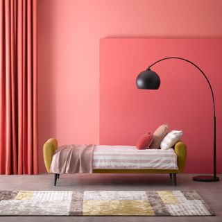 A mustard sofa bed with pink and white striped bedding in a coral pink room with a large black standing lamp