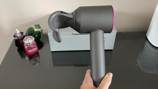 Dyson Supersonic hair dryer with fly away attachment being held above a dressing table