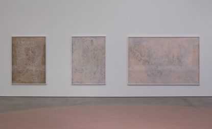 Three beige paintings hanging on a white wall