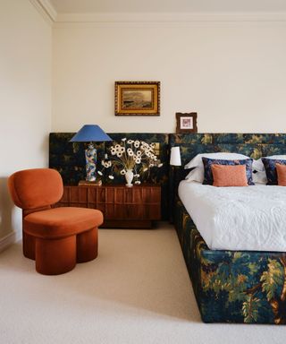 neutral bedroom with a wide wall-to-wall upholstered headboard in a green tapestry leafy print accessories with vintage furniture