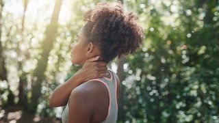 A runner in the woods massages her neck