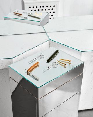 A mirrored table with a wooden handled shaving razor, two scissors, a black comb and two hair clips.