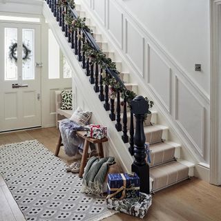 Garland of eucalyptus and pine cones decorated on white staircase with black balustrade next to wrapped gifts on wooden floor