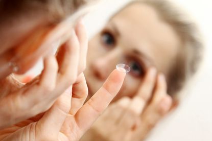 A woman puts a contact lens in her eye.