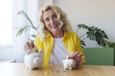 Happy senior woman saving money in piggy banks at table