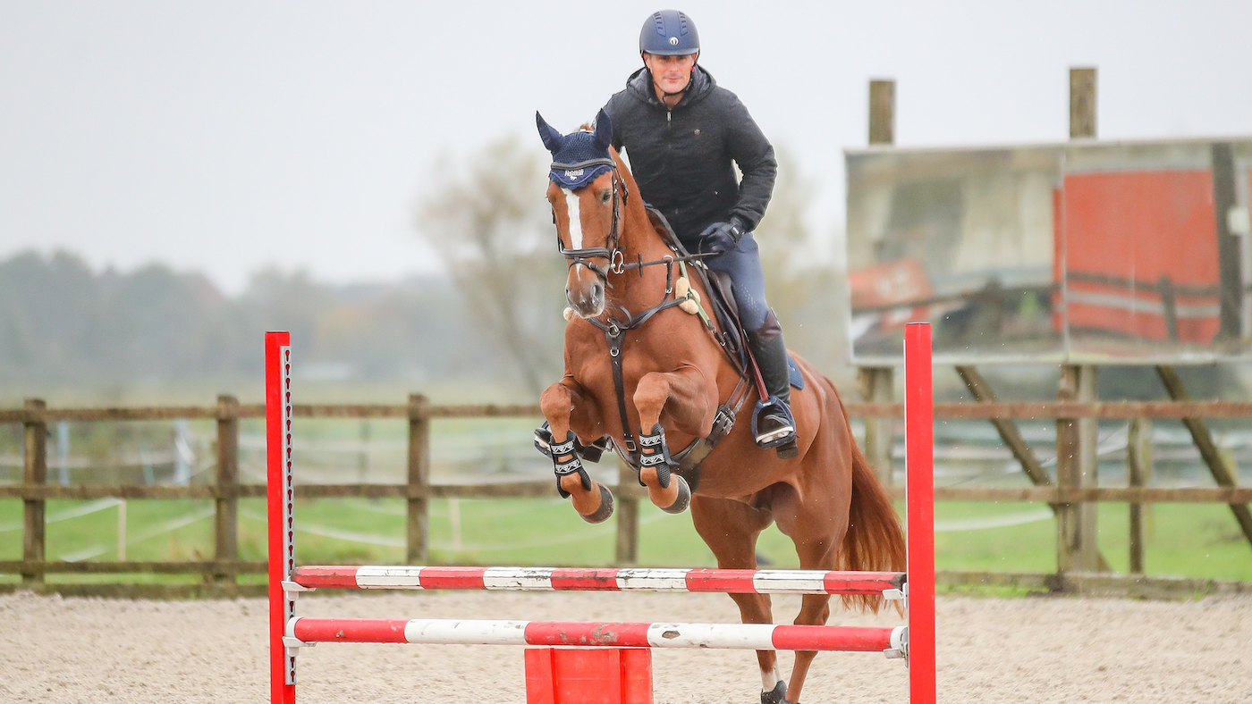 Alex Bragg training chestnut horse over a jump to improve straightness