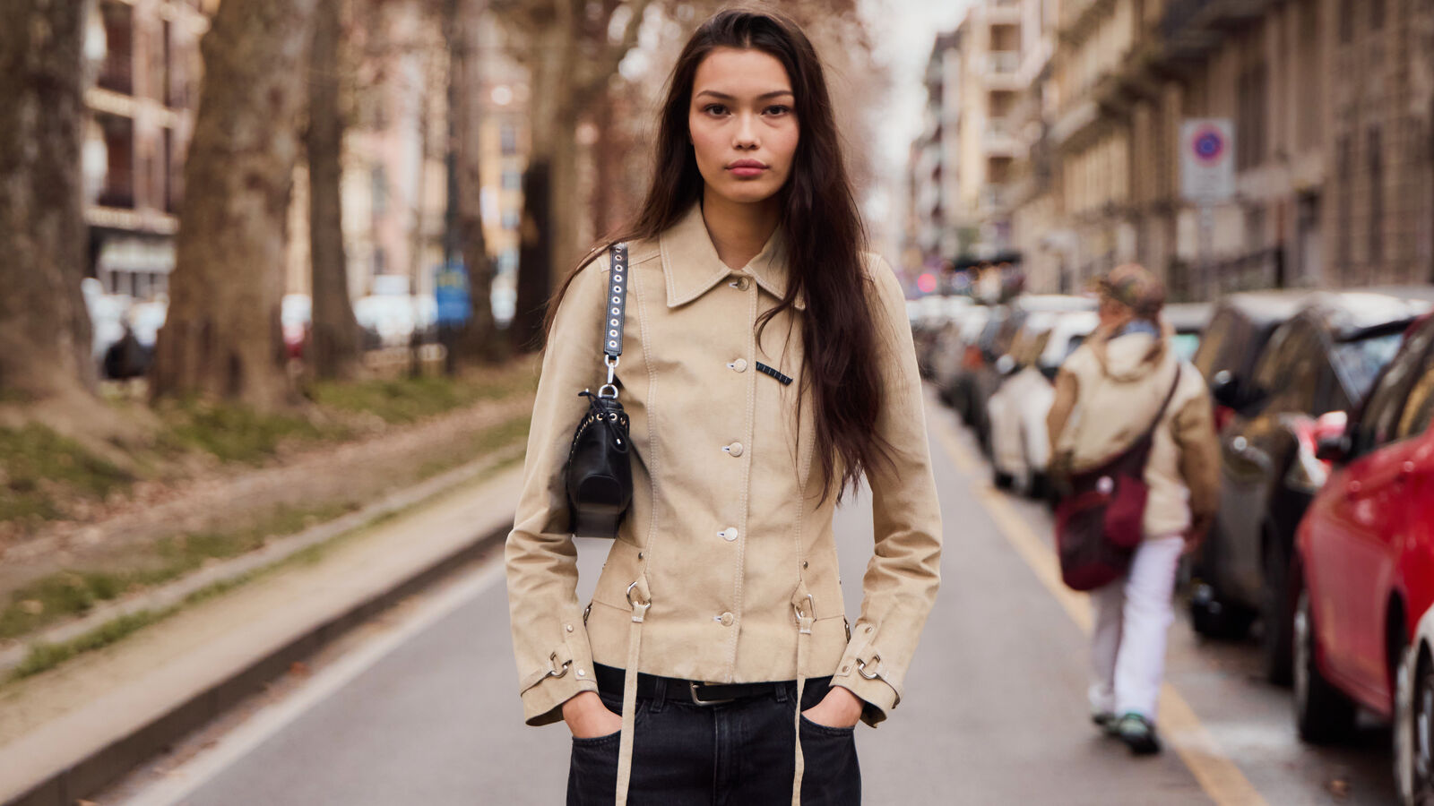 Woman wears cropped fitted trench style coat and black trousers while posing in the street. 