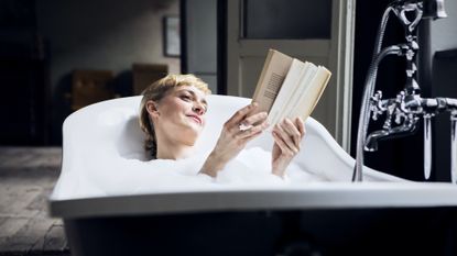 Portrait of relaxed woman taking bubble bath in a loft reading a book - stock photo