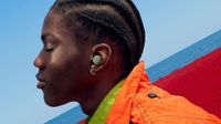 A side-on view of a person wearing the new Olive green Pixel Buds Pro 2 standing in front of a red and blue background