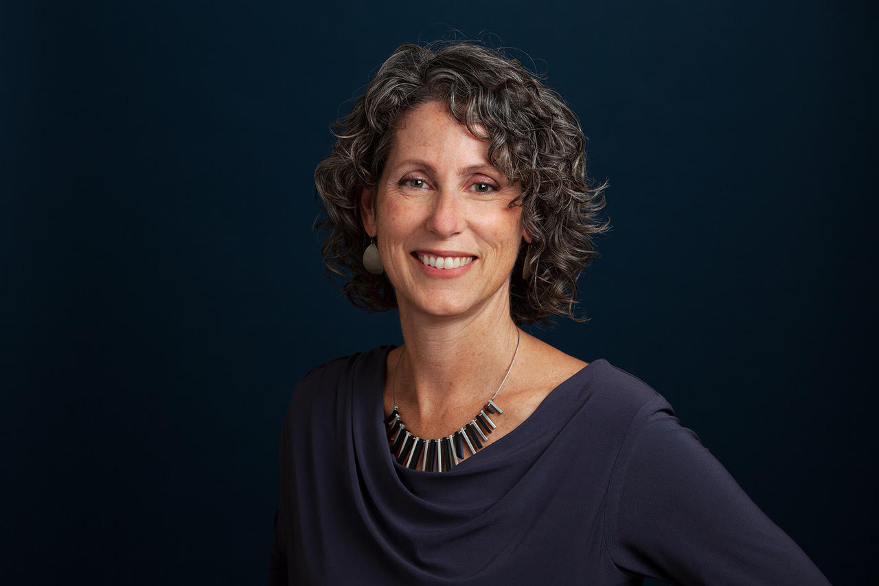 Headshot of woman in blue top with jaw-length dark hair on a navy background