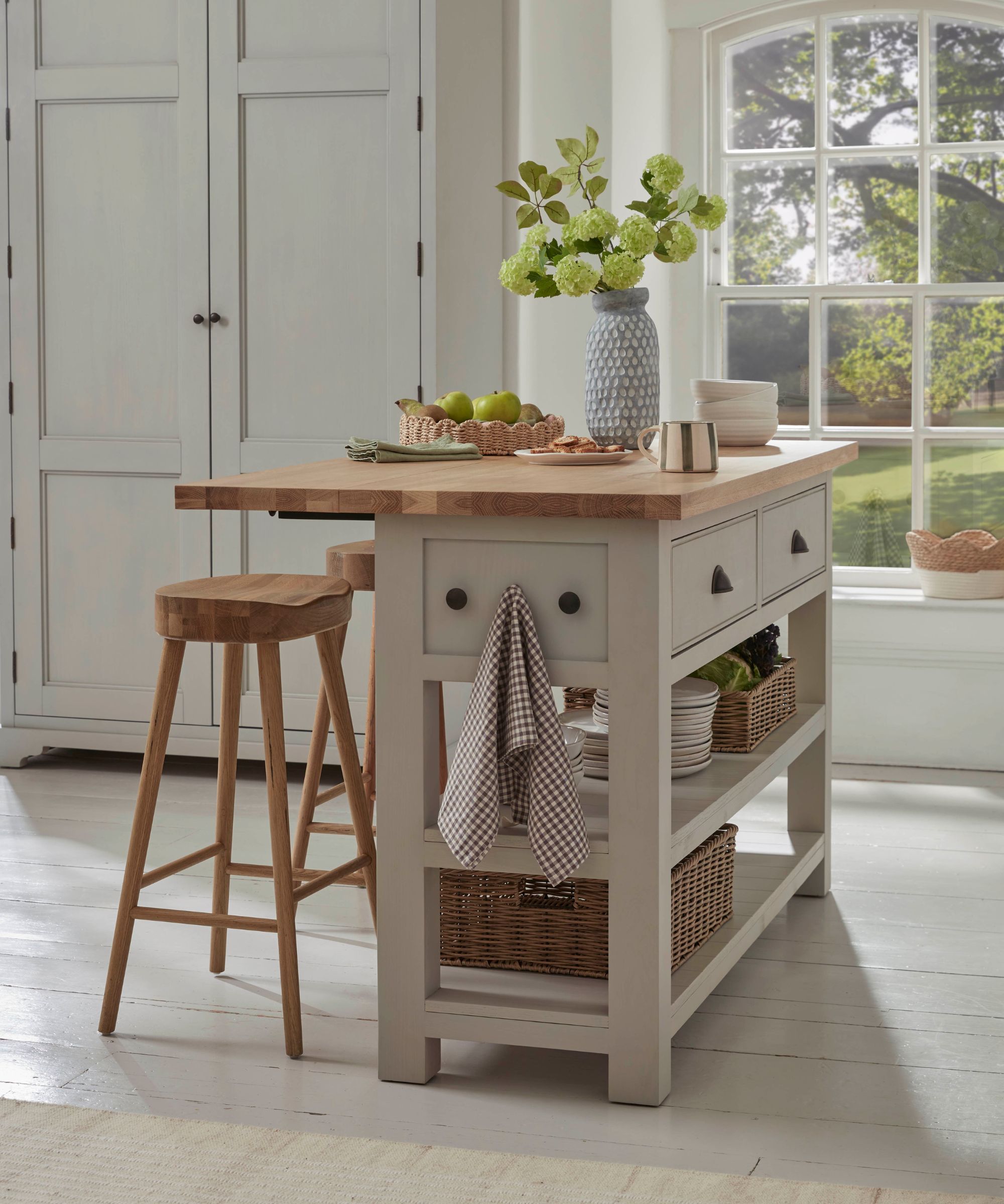 A light-filled kitchen with a painted island, chunky wooden worktop, open shelving and basket storage, combining charm with everyday functionality.