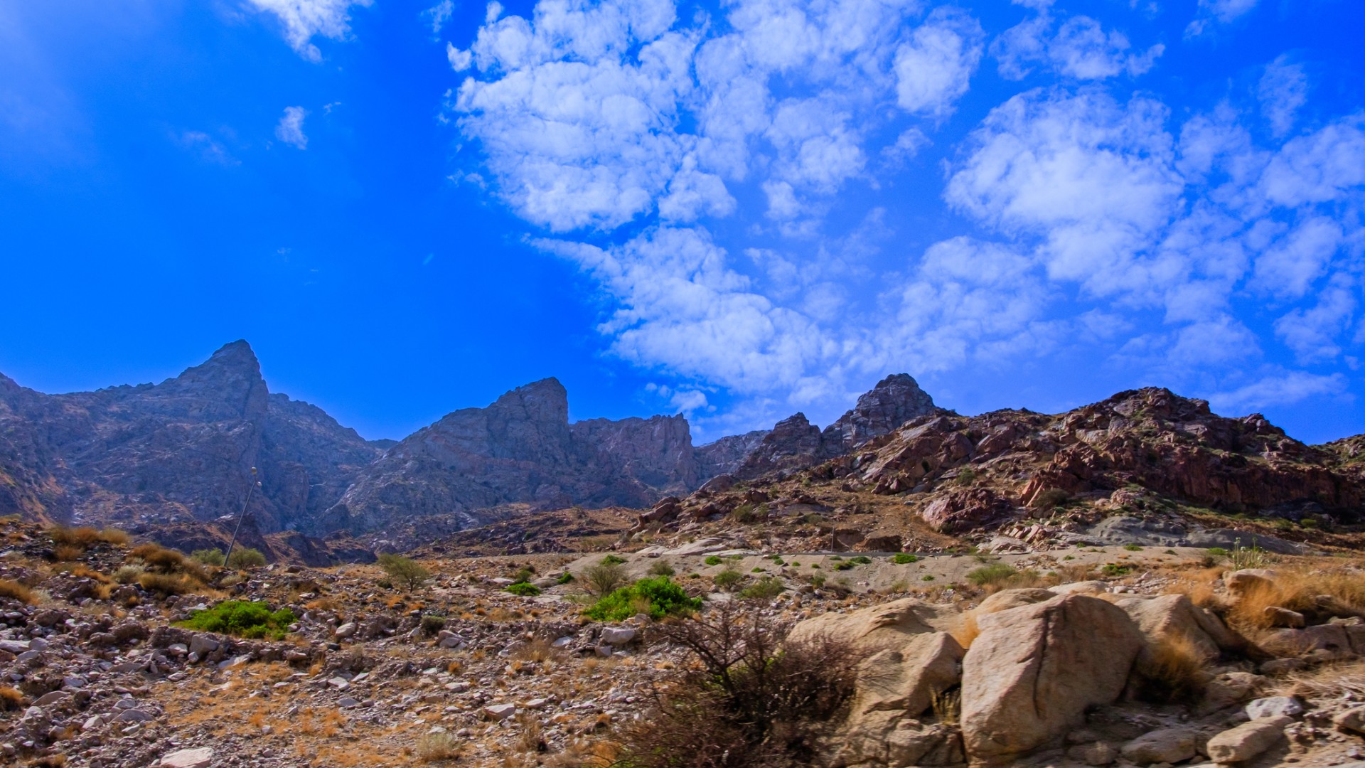 Majestic rocky mountains under a vibrant blue sky with scattered clouds, showcasing a rugged desert landscape.