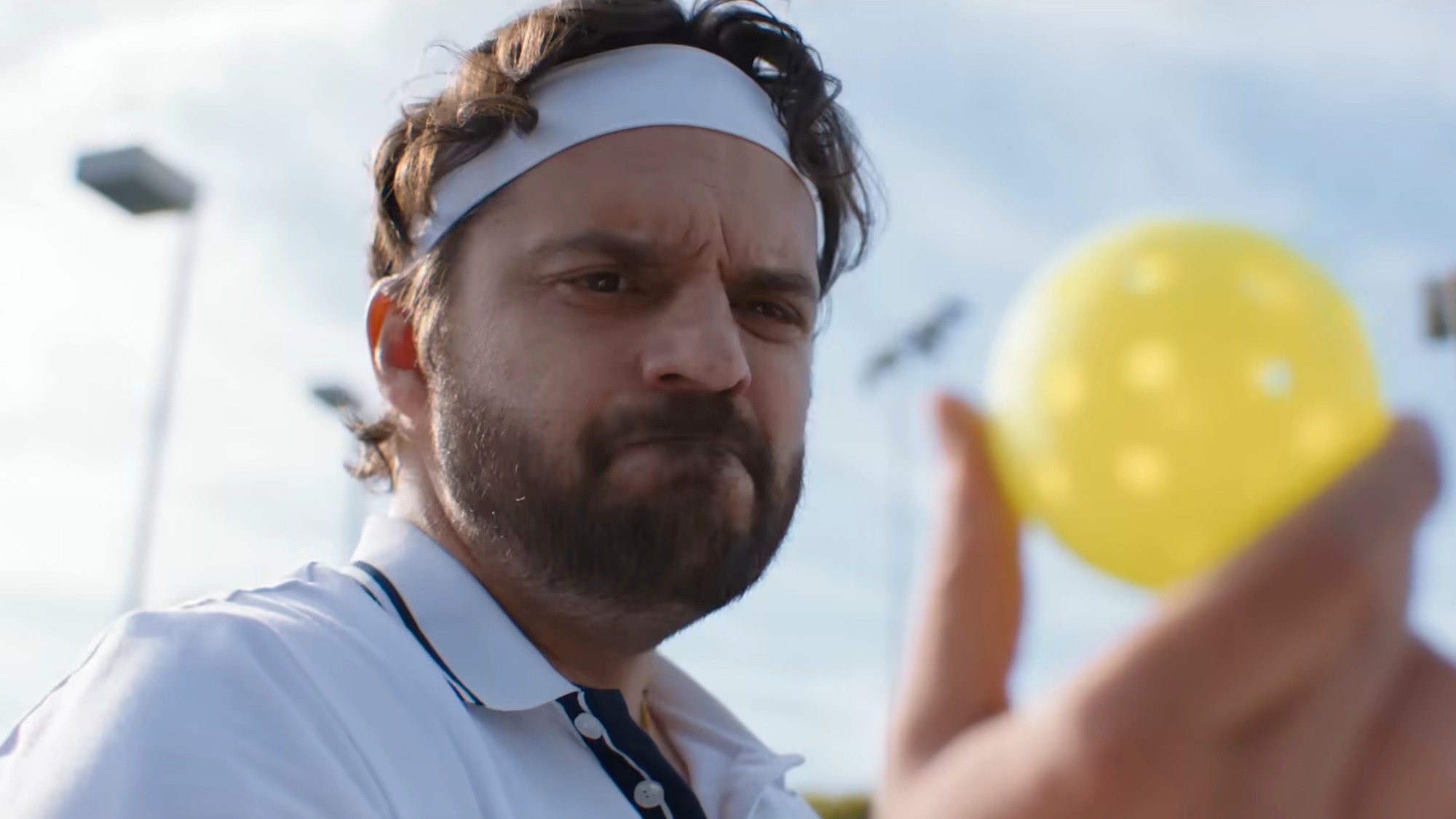 Jake Johnson as Dusty Boyd is shown in The Dink, looking at a pickleball with disdain.