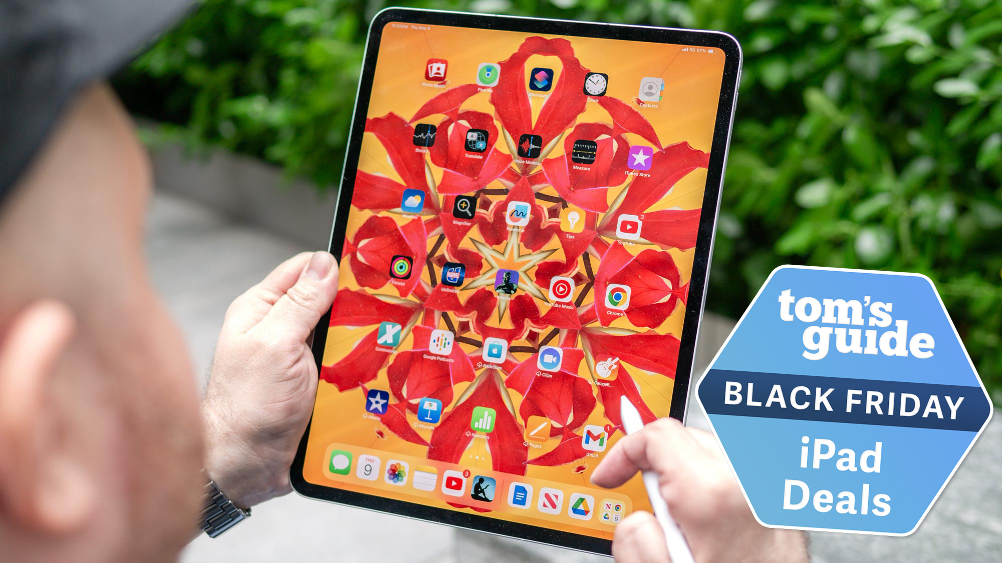 A person holding an iPad Pro M4 on the home screen with an orange and red wallpaper. The person is holding an Apple Pencil. There is a Tom&#039;s Guide badge in the right lower corner.