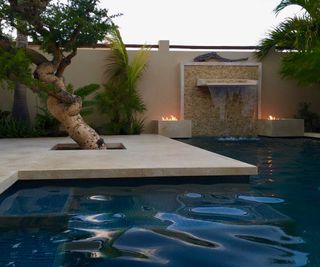 paved backyard with pool, fire features, and tree by Gardenart Group