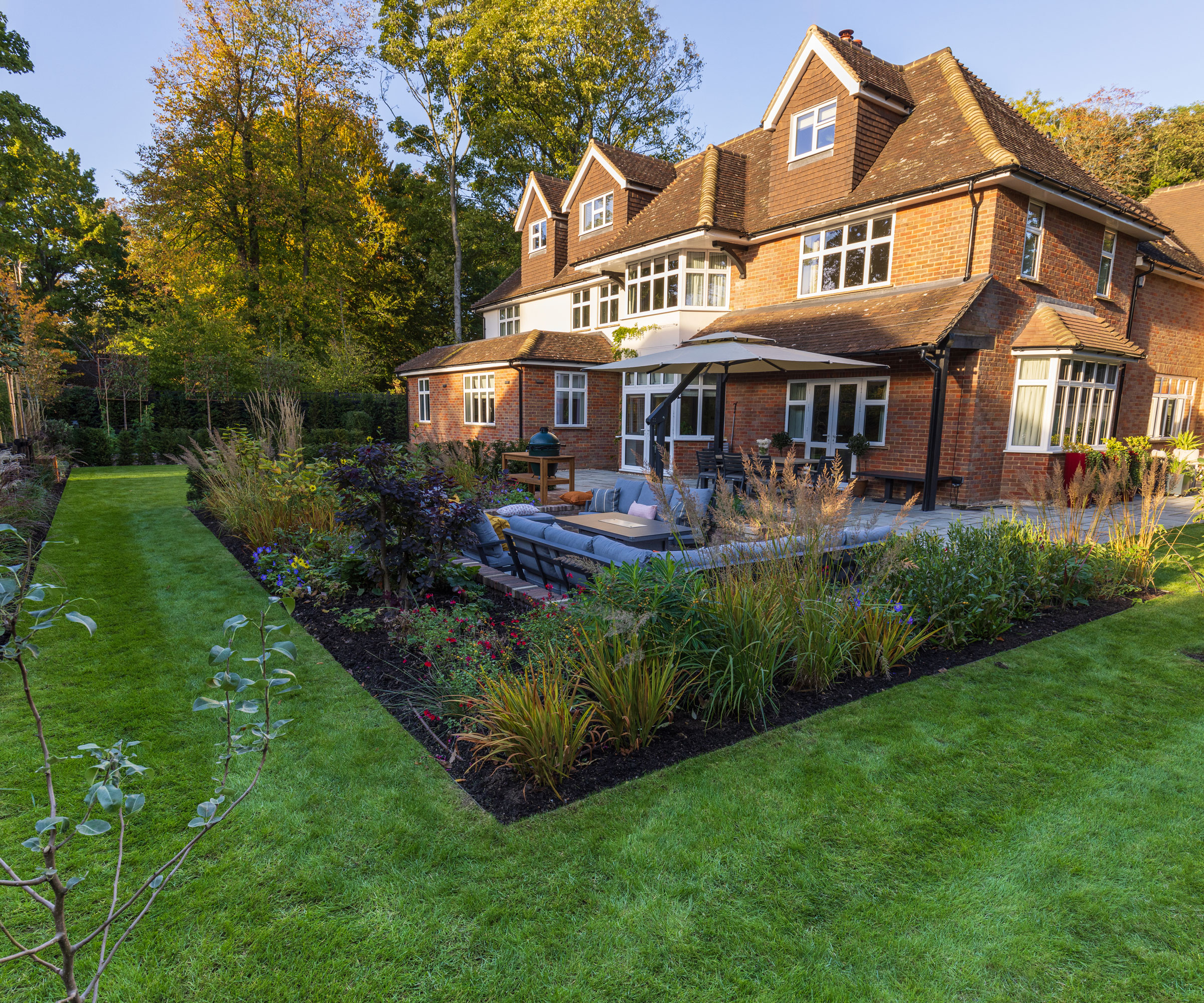 L-shaped garden with entertainment area, trees, lawn and flowerbeds