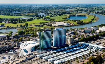 The Dutch city of Arnhem just got a brand new station, courtesy of Amsterdam-based architecture firm UNStudio. An aerial view of Arnhem Station with three train lines and two buildings next to them and a golf course behind the buildings.