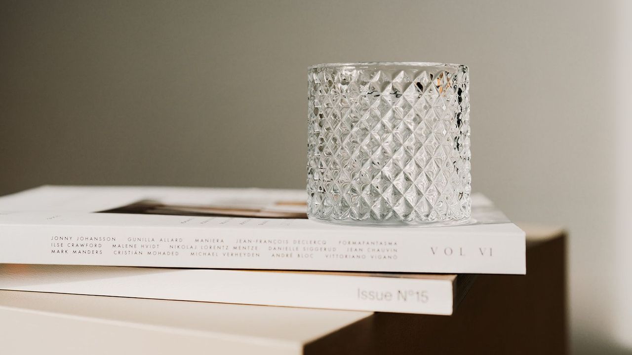 A textured short drinking glass on top of two high-end magazines on a cube side table. neutral plain background