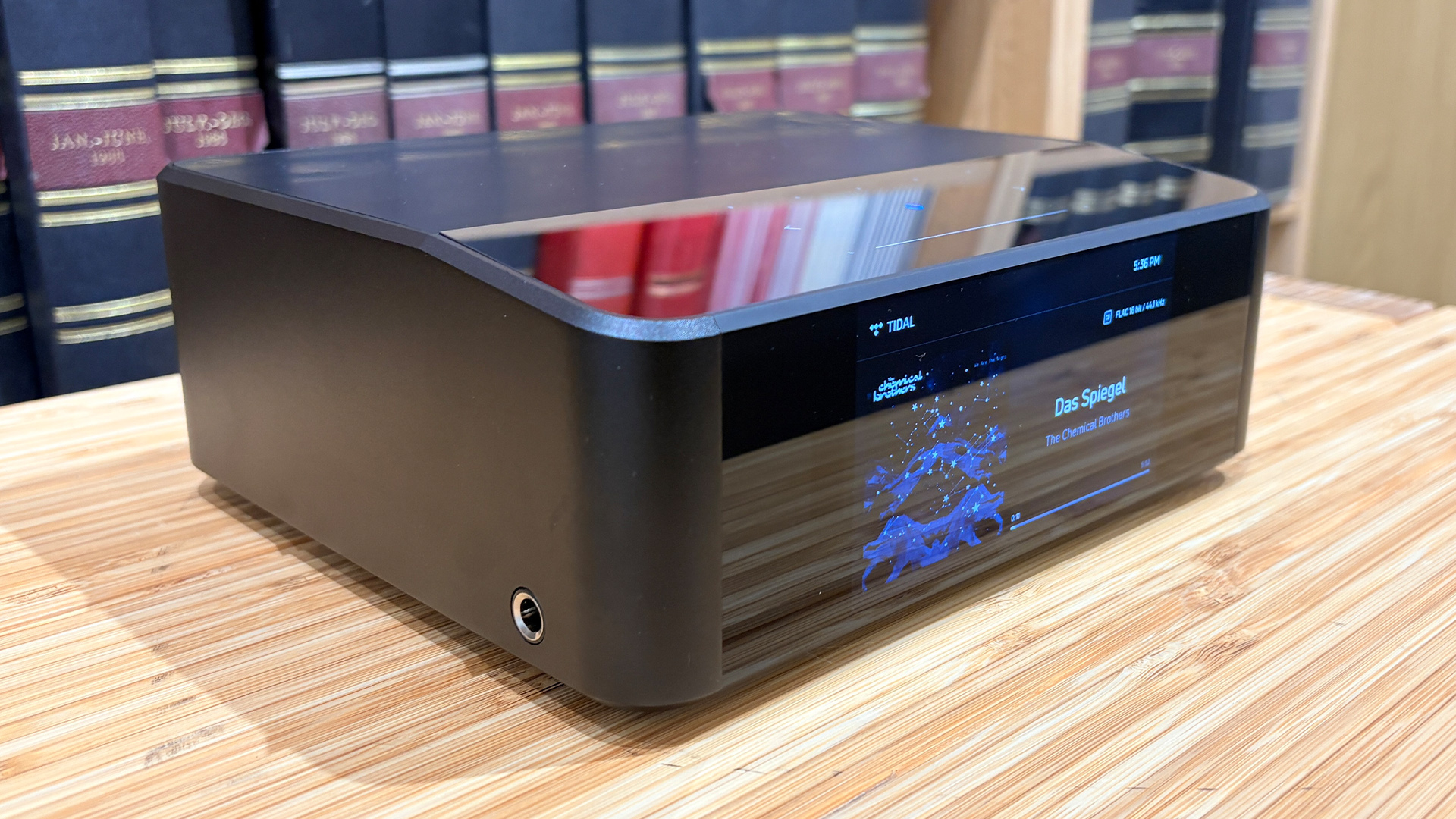 Bluesound Node Icon music streamer on wooden hi-fi rack in front of bookcase slight side angle