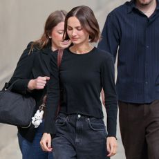 Maude Apatow wears black baggy jeans with a black longsleeve top and black heeled ballet pumps.