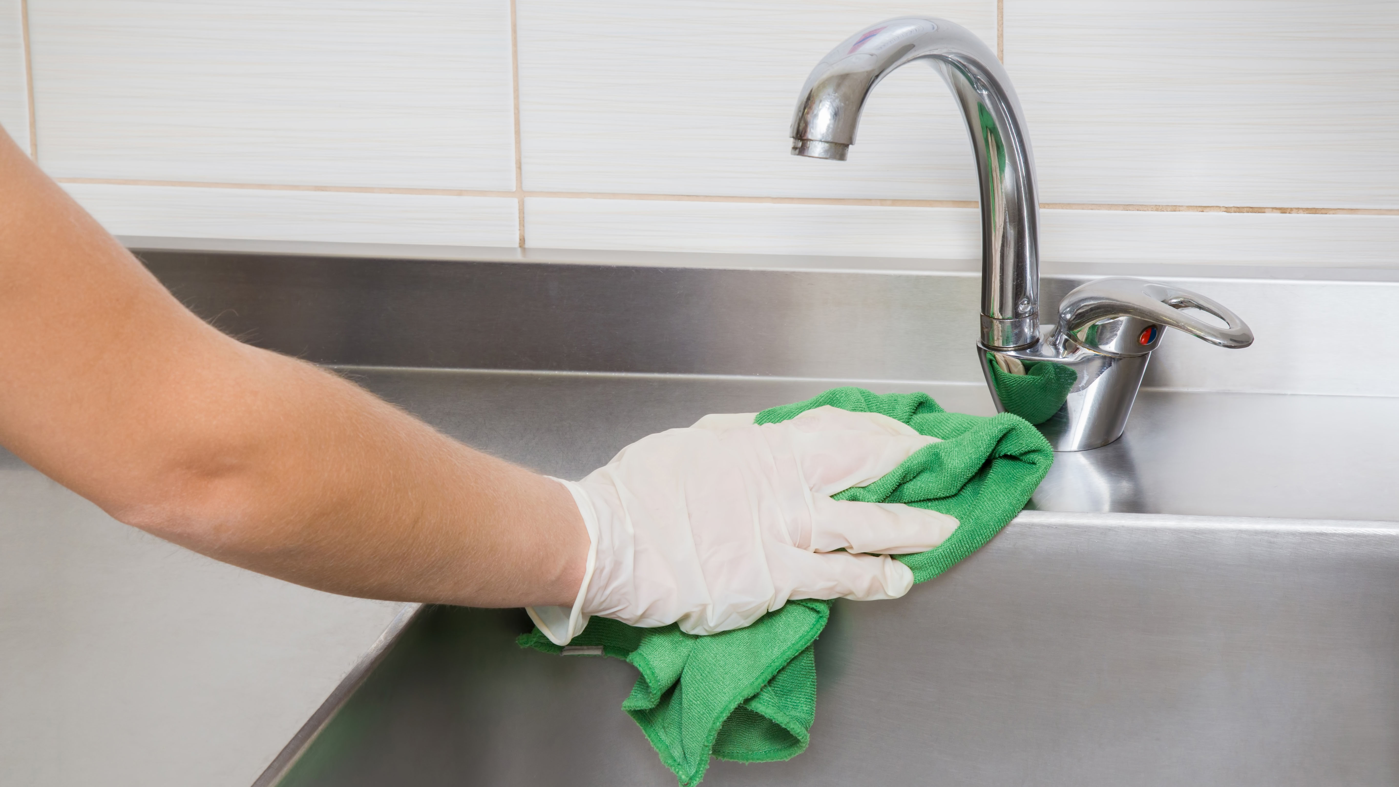 A stainless steel sink being cleaned with a cloth while wearing gloves