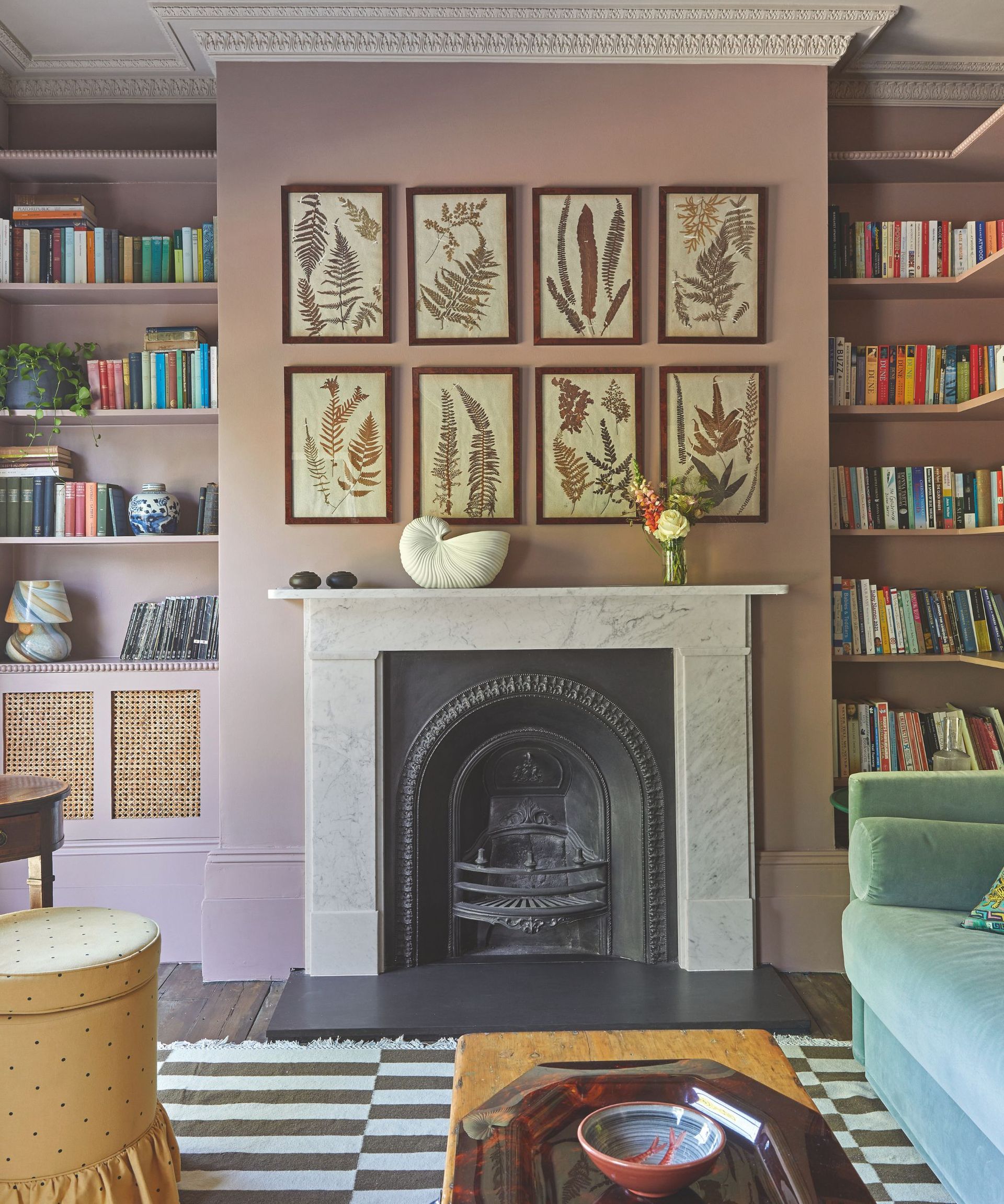 Maximal living room with botanical prints above fireplace and striped rug and bookshelves