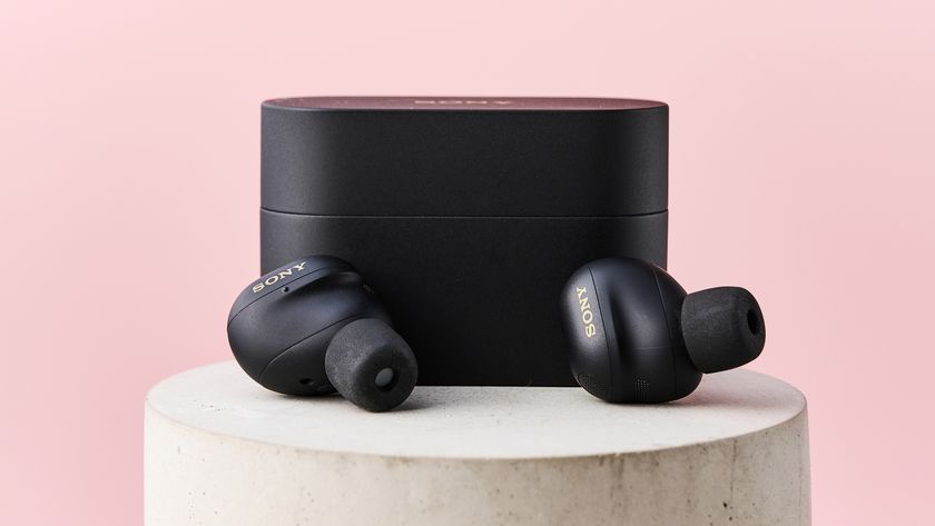 The Sony WF-1000XM6 lying in front of their case on top of a stone pillar in front of a pink background.