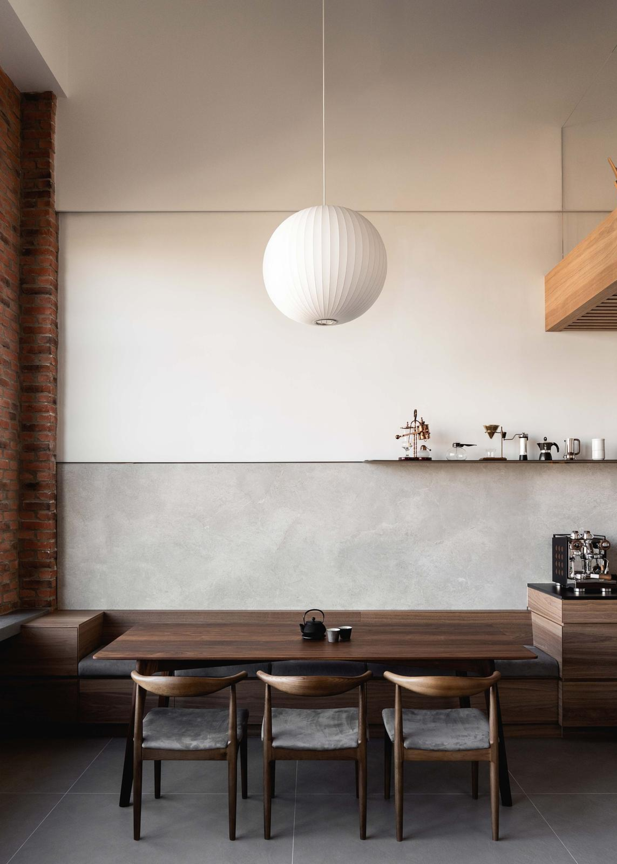 A dining area with banquette seating and wooden chairs beside a coffee bar with a paper lantern above