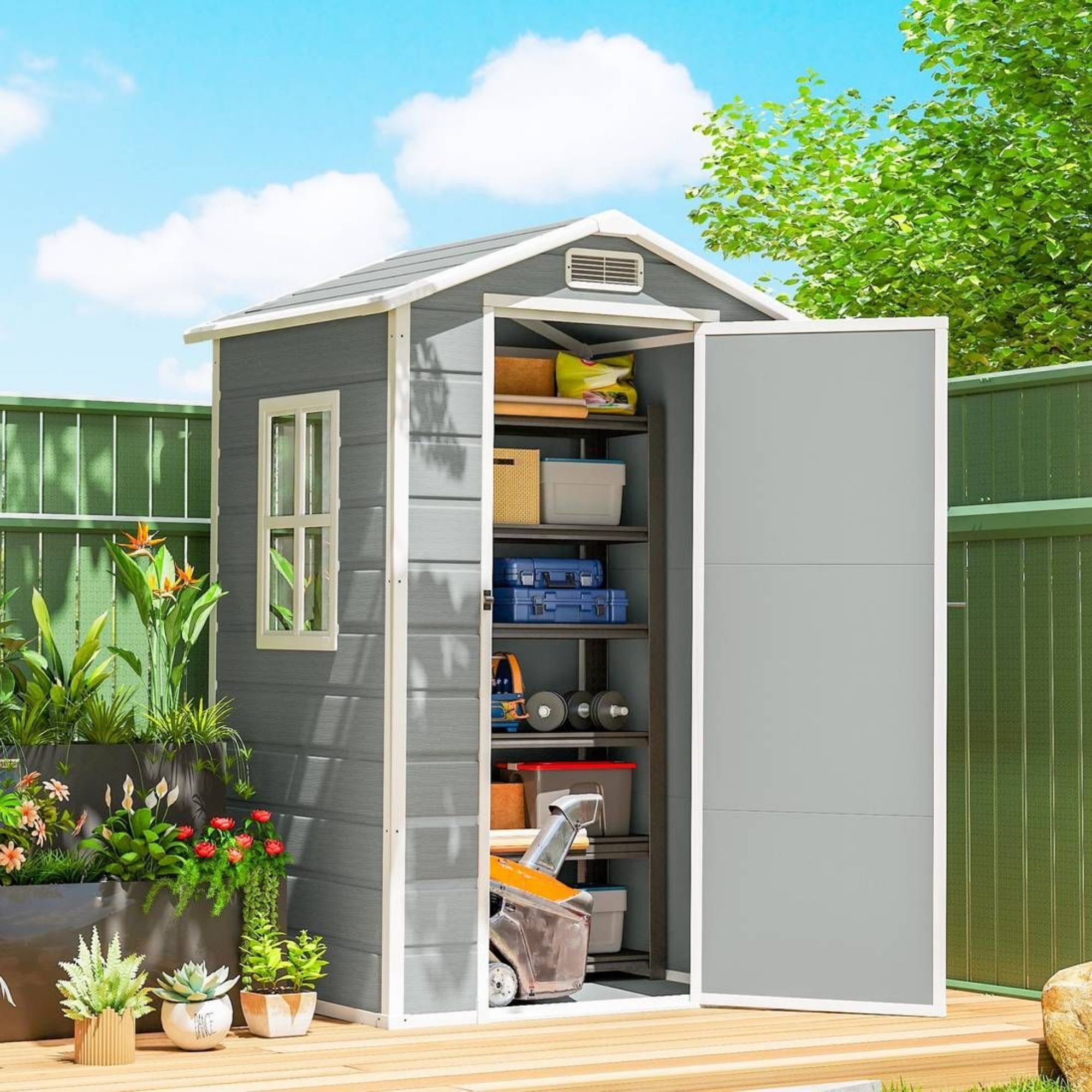 grey plastic shed sitting on decking in a garden, next to lots of pots with plants