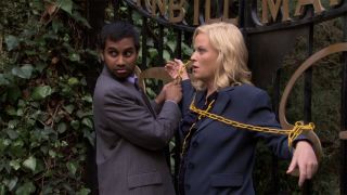 Tom Haverford (Aziz Ansari) chains Leslie Knope (Amy Poehler) to a fence in Parks and Recreation